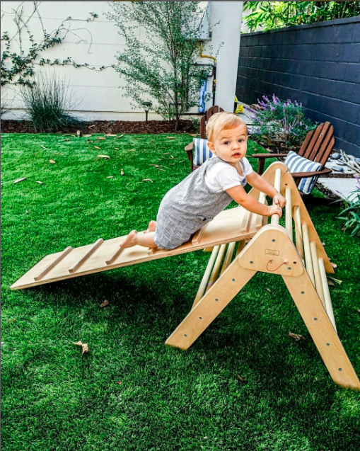 baby climbing on pikler triangle in backyard