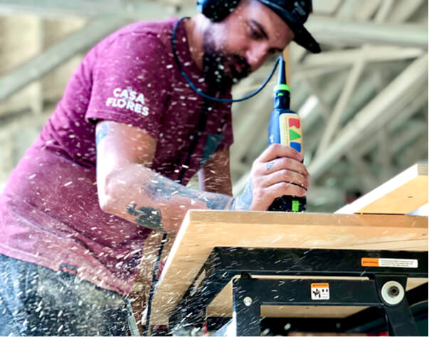 Person using a power tool on a wooden surface with visible wood shavings.