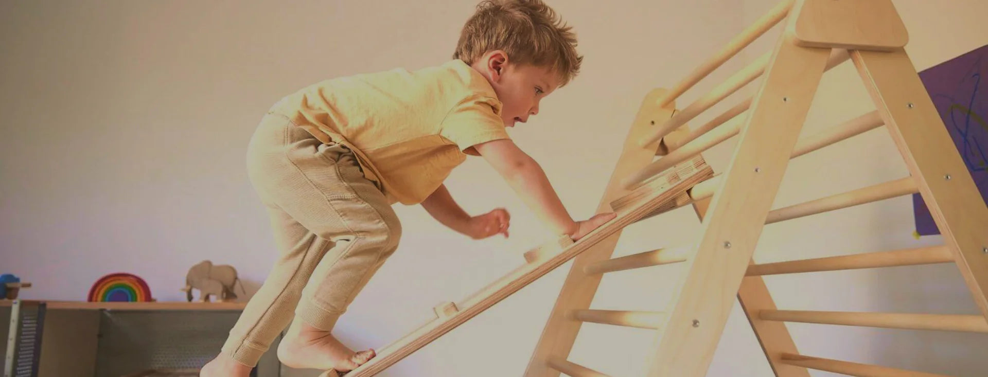 Child climbing a pikler triangle in a room with toys on shelves.
