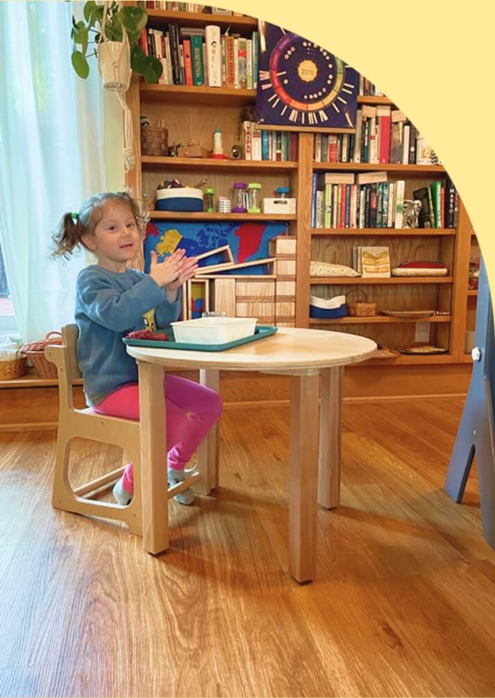 Child sitting at a small table in a room with bookshelves and toys.