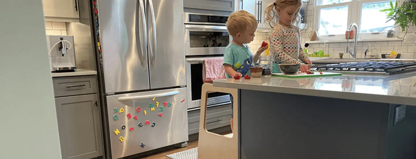Two children playing in a modern kitchen with stainless steel appliances.