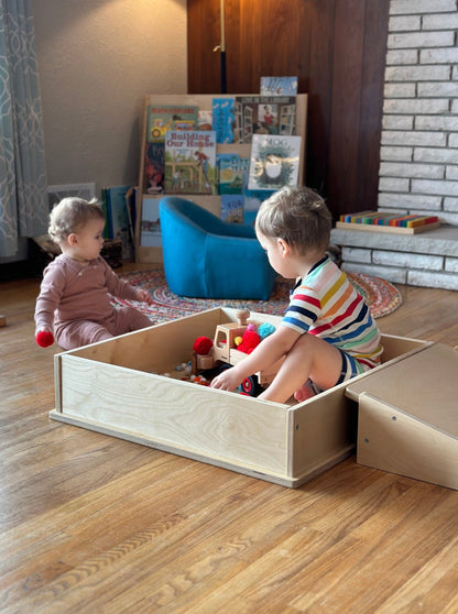 little boy playing in a play box by flipping over a pikler platform