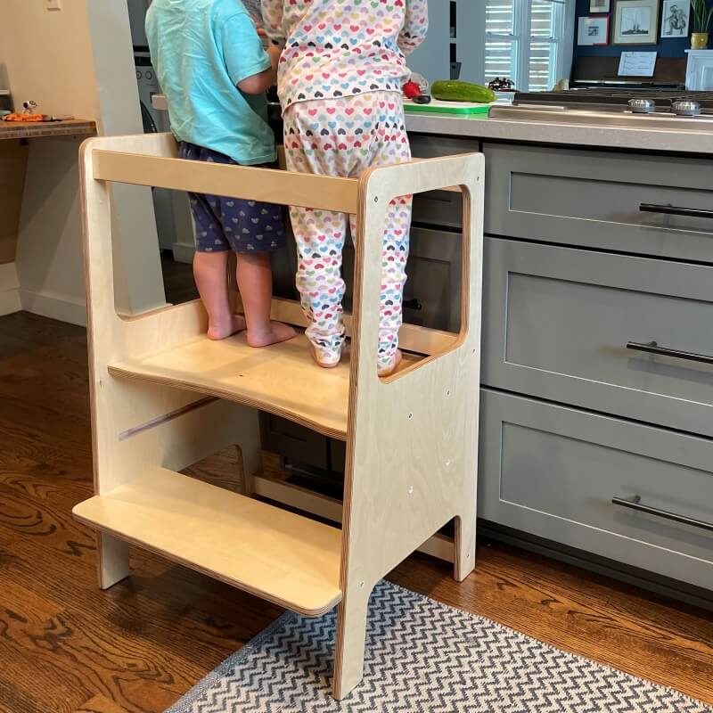 two children in learning tower working in kitchen